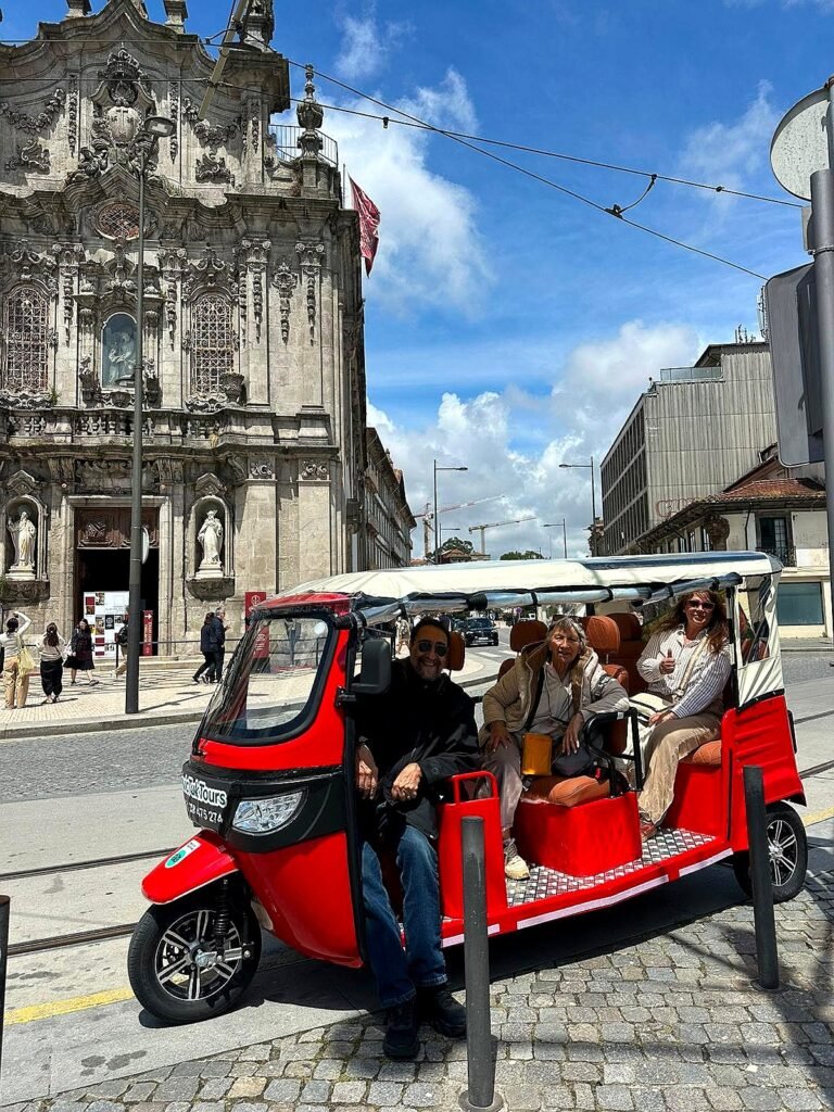 Red electric tuk tuk with guests in front of Carmo Church, Porto