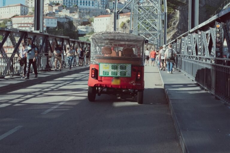 Red electric tuk-tuk crossing the Dom Luis I Bridge in Porto